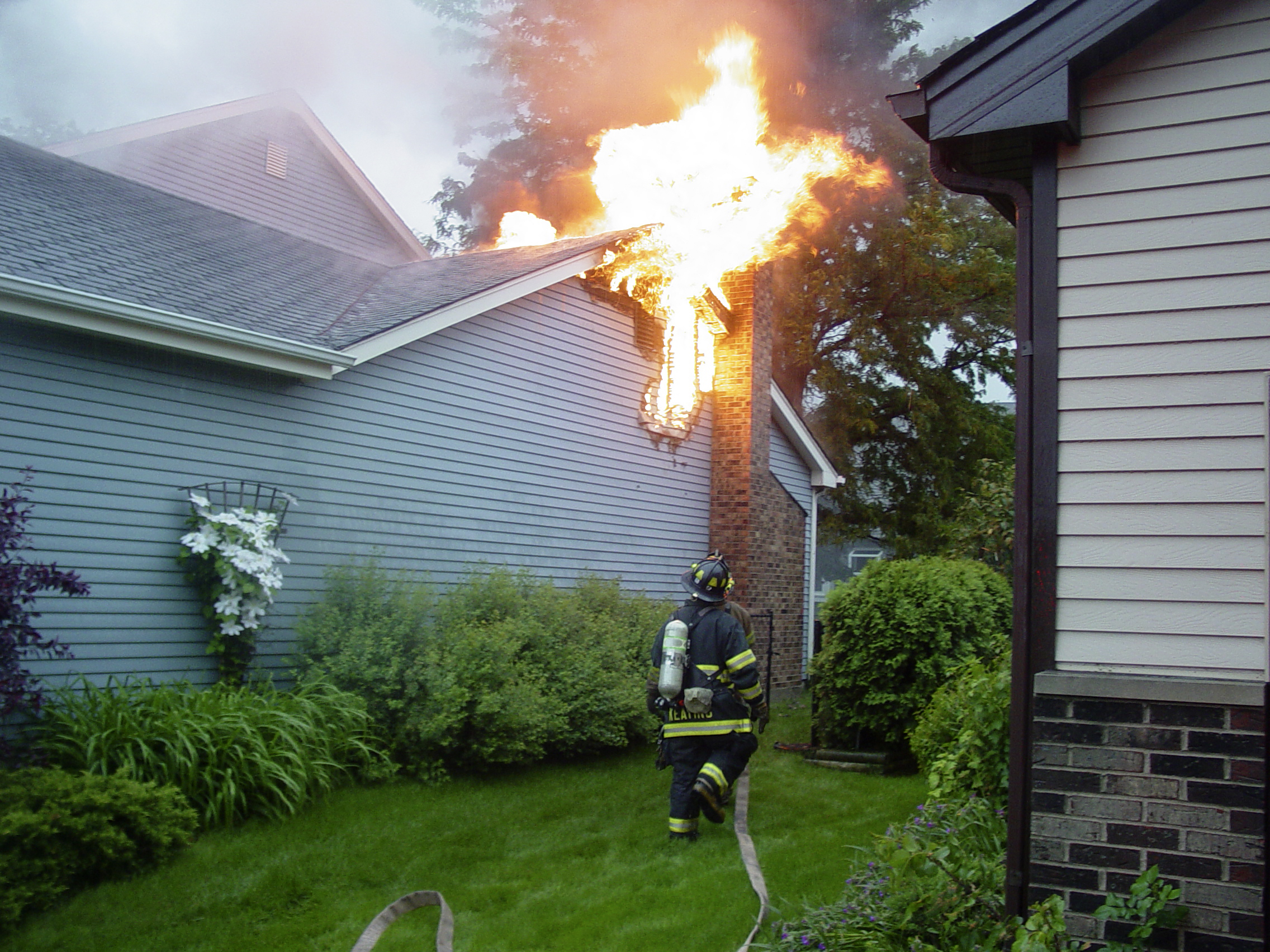 Firefighter battling flames breaking through the roof of a house