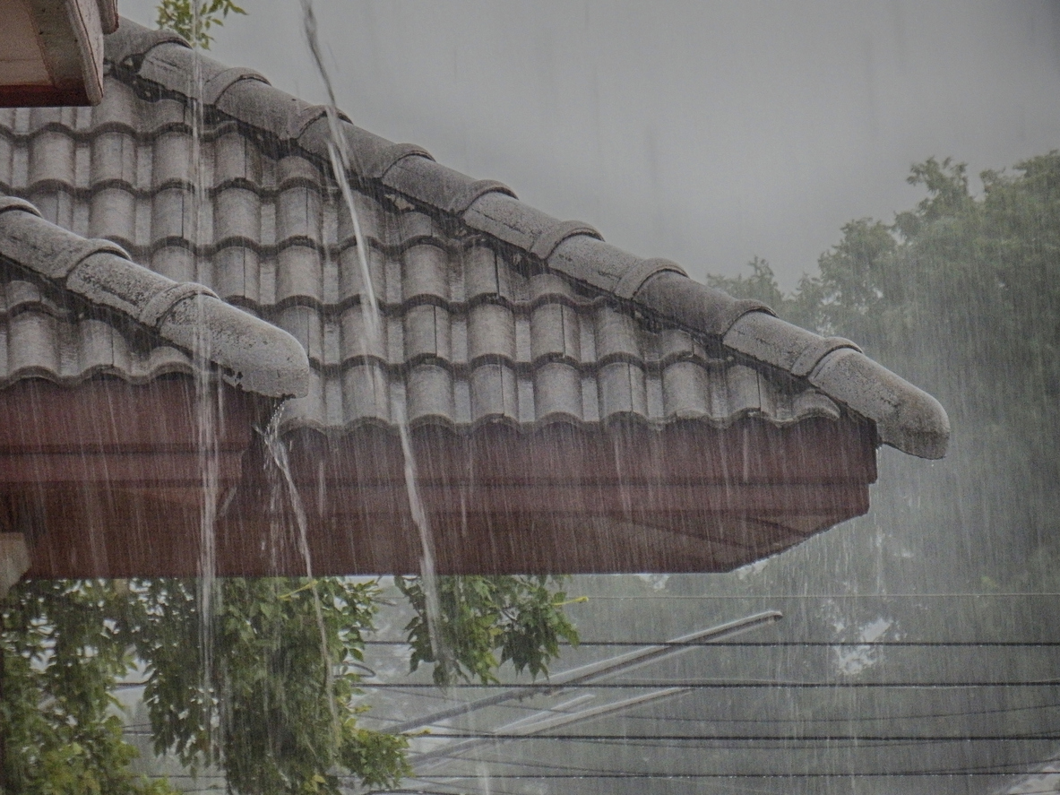 Heavy rainfall pouring down on the roof and siding of a house