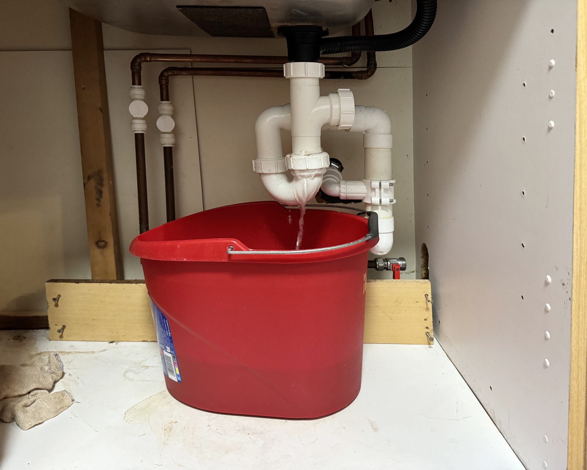 Water leaking from a pipe under a sink into a red bucket