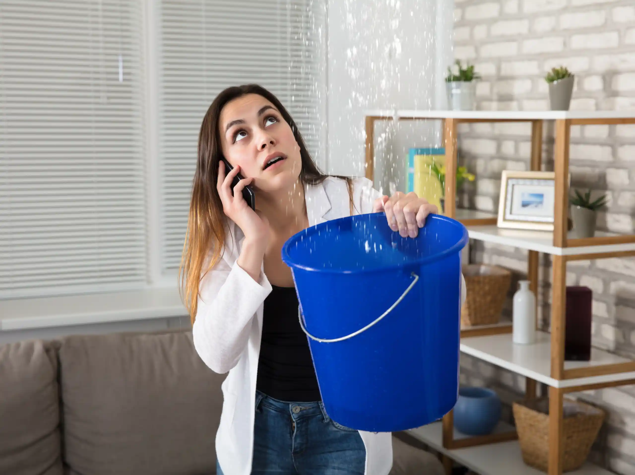 Homeowner calling Right-Now Restoration while catching a ceiling leak in a bucket